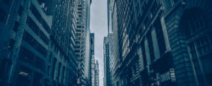 Tall skyscrapers line a narrow city street under a cloudy sky.