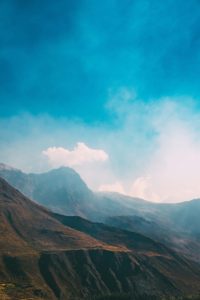 A serene mountain landscape under a bright blue sky with clouds.