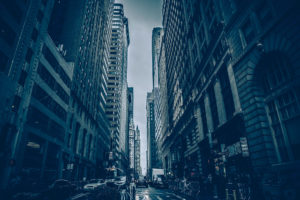 Urban street flanked by tall buildings under a moody sky.