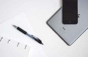 Pen resting on paper beside a tablet and a smartphone on a desk.