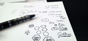 Various hand-drawn logo sketches and a pen on white paper.