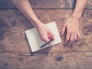 A person writing in a notebook on a wooden table.