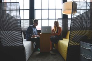 Two colleagues discussing work in a modern office lounge with a laptop.