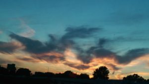 Sunset with colorful clouds over silhouetted trees and buildings.