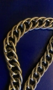 Close-up of a thick gold chain necklace on a dark background.