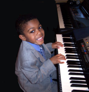 Young boy in a suit playing the piano and smiling.