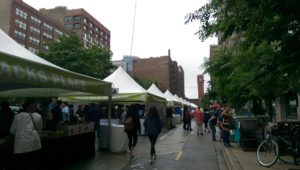 Outdoor market with white tents and visitors on a city street.