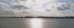 Calm water reflecting bright sunlight under a cloudy sky.