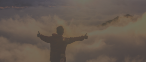 Person with arms outstretched facing a cloudy sky at sunset.