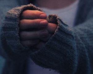A small frog held gently in hands with cozy sweater sleeves.