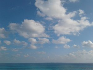 A serene ocean under a partly cloudy blue sky.