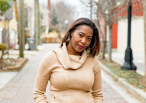 Woman in a beige sweater smiling outdoors on a city street.
