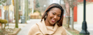 Smiling woman outdoors wearing a beige sweater.