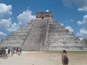 Ancient stepped pyramid under a bright blue sky with scattered clouds.