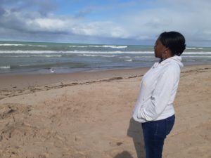Person in a white jacket gazing at the ocean on a cloudy beach.