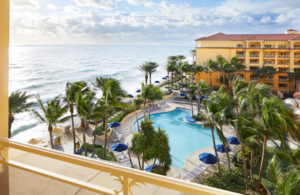 Resort pool area surrounded by palm trees near the ocean at sunset.