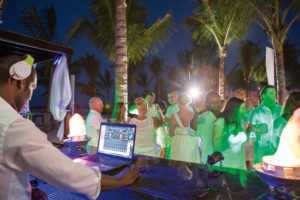 DJ playing music at an outdoor nighttime party with dancing crowd.