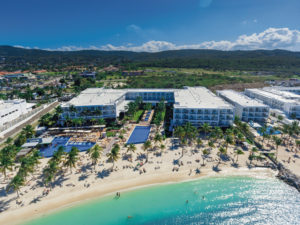 A luxurious beachfront resort with pools and sun loungers by clear turquoise water.