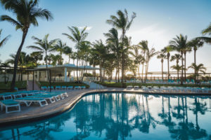 A serene poolside view at sunset with palm trees and lounge chairs.