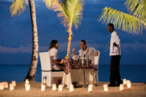 Couple enjoying a romantic beach dinner with a waiter serving them.