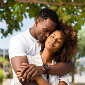 Couple embracing lovingly outdoors under green leaves.