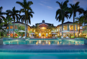 Luxurious tropical mansion at sunset with a large pool and palm trees.
