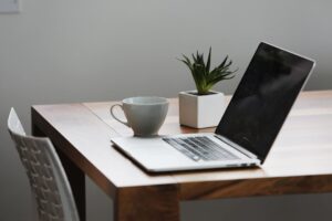 Minimalist workspace with laptop, coffee cup, and small plant on wooden desk.
