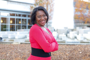 Smiling woman in a bright pink sweater posing outdoors with arms crossed.